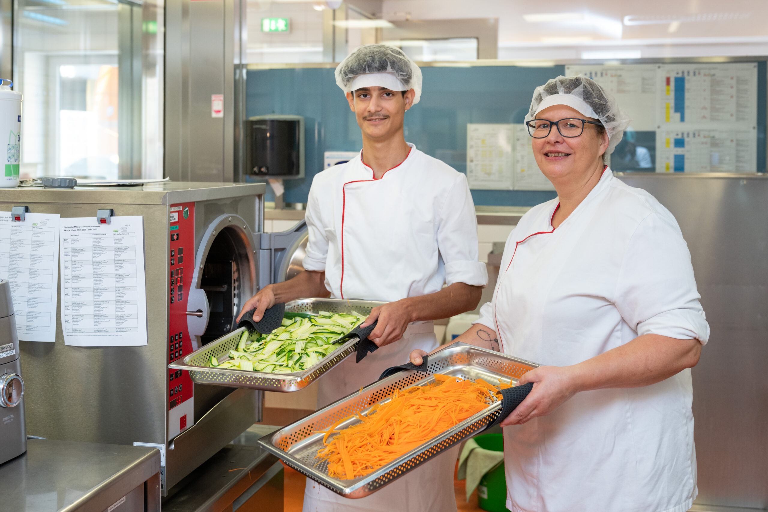 Zwei Personen des Küchenpersonals halten Behälter mit Karotten und Zucchini