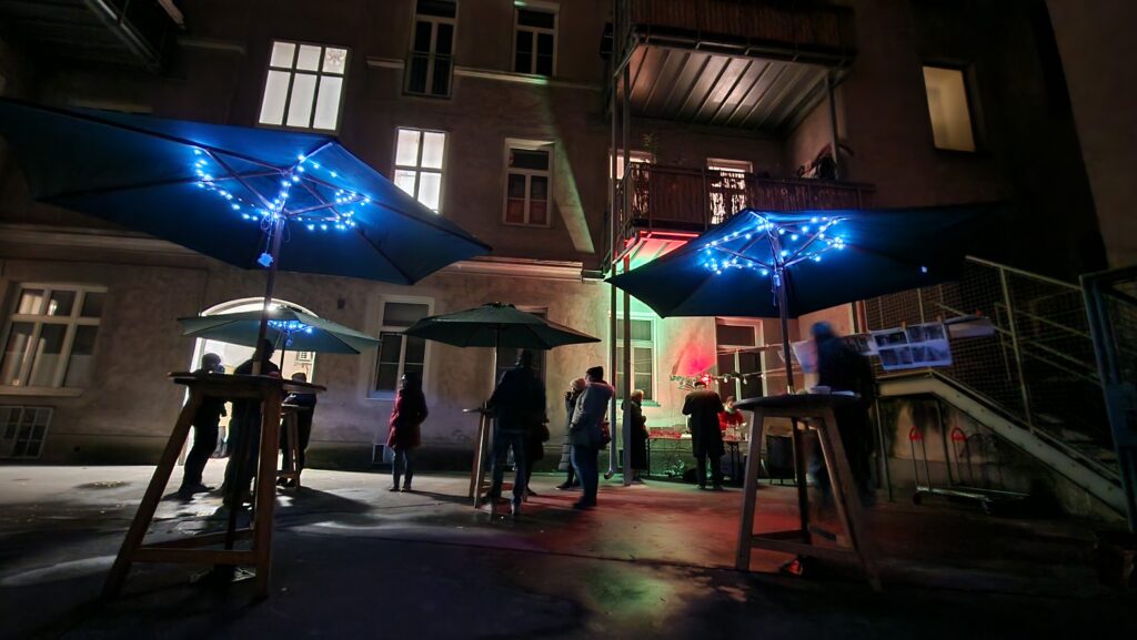 Punschfest mit Mieter:innen im Innenhof mit Stehtischen, Schirmen und Beleuchtung