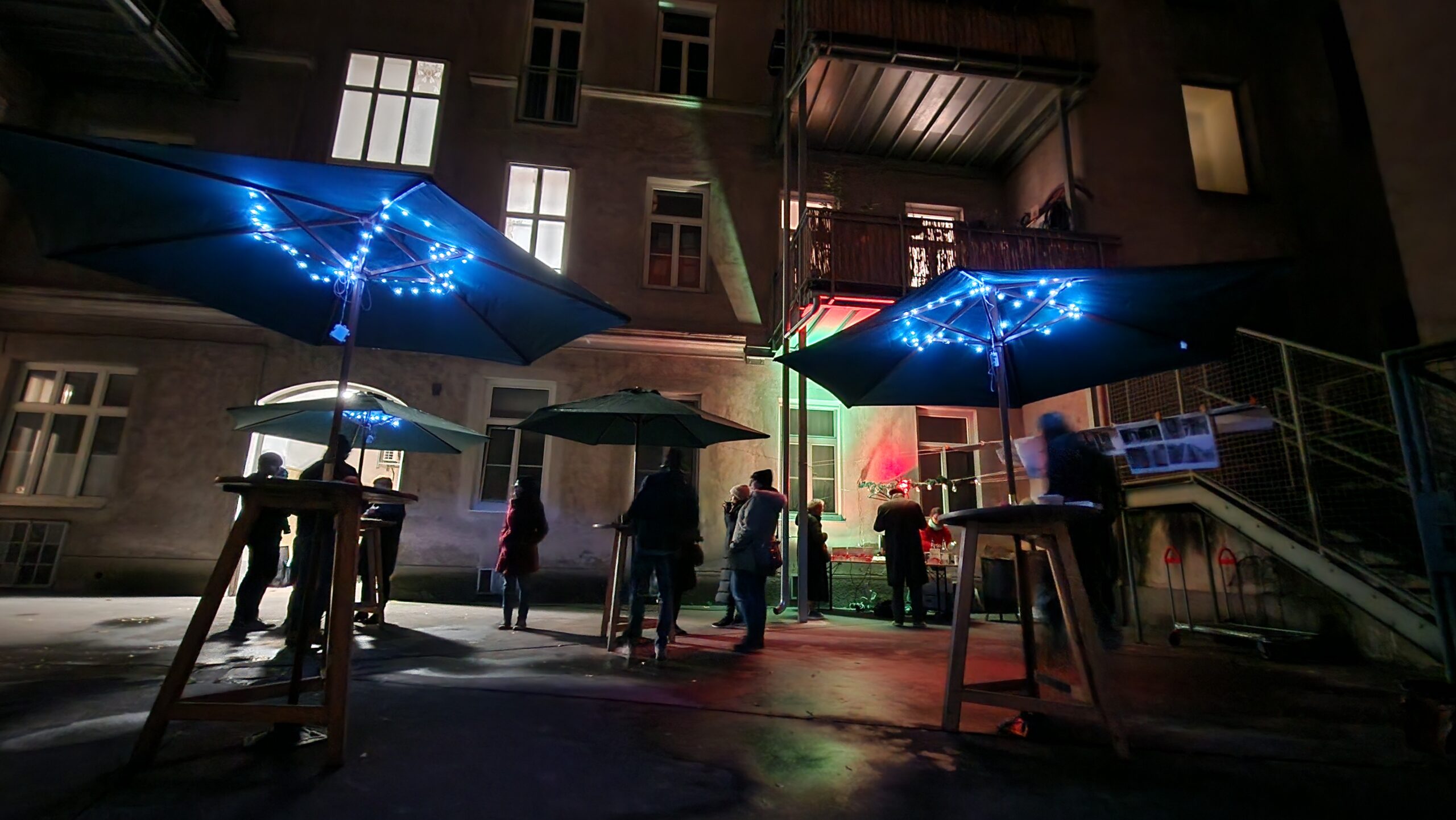 Punschfest mit Mieter:innen im Innenhof mit Stehtischen, Schirmen und Beleuchtung