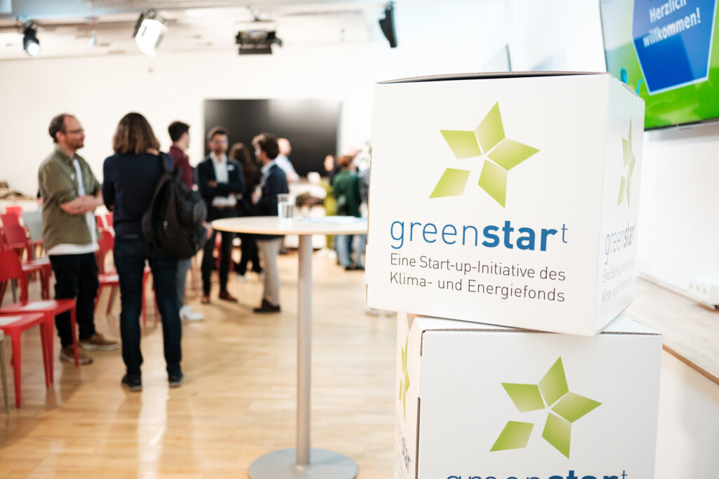 Würfel mit dem greenstart-Logo bei einer Veranstaltung mit Personen im Hintergrund