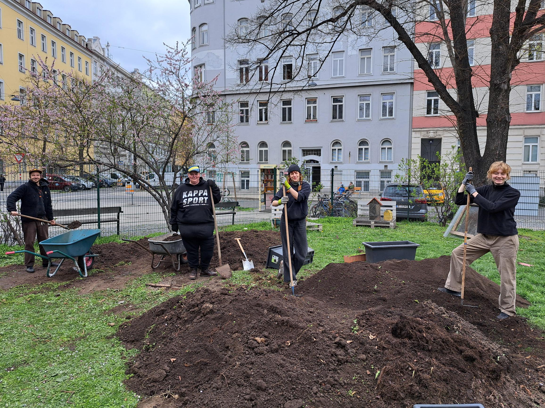 Vier Personen aus dem Team auf Erdhaufen. Sie graben den Garten um, um Platz für neue Hochbeete zu schaffen.