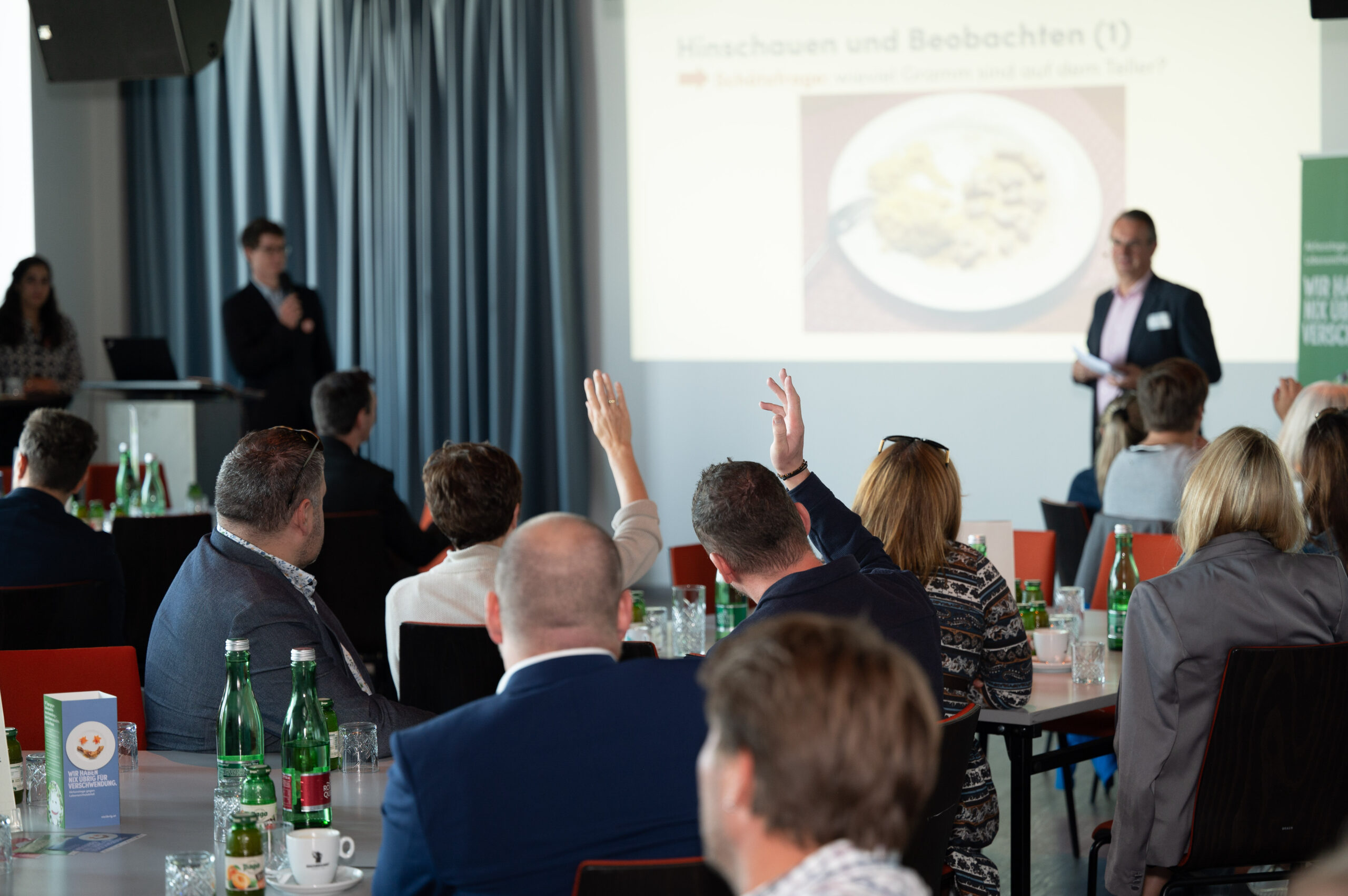 Vortrag von zwei UAW-Mitarbeitern, Personen im Publikum heben die Hände